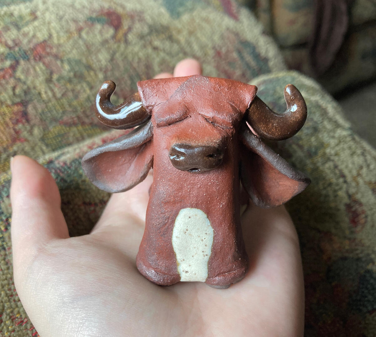 A ceramic cow being held up by a hand.